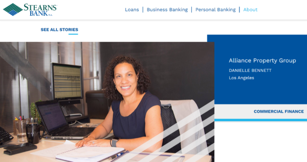 An image of a woman smiling and sitting at her desk.